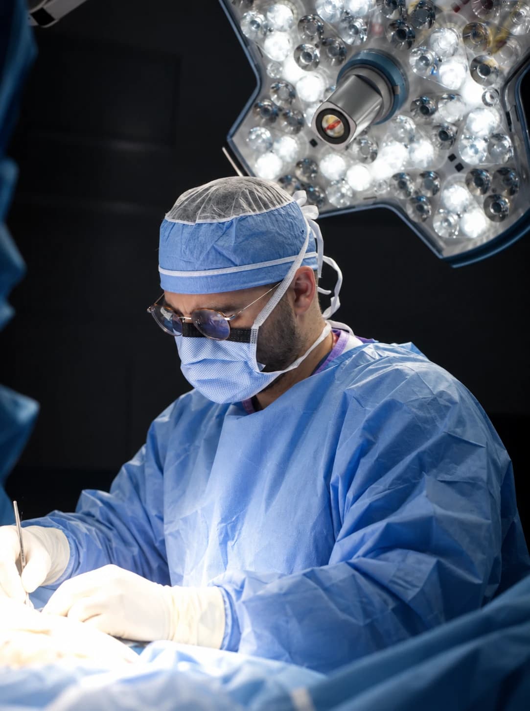 Dr. Efe Ozturk in surgical cap, mask and gown, operating under surgical lights